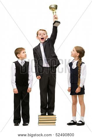 Full-length portrait of little boy standing with gold cup at pile of books among other children, isolated on white. Concept of teamwork and cooperation