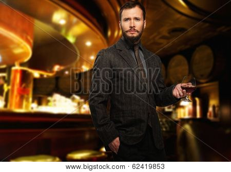 Handsome well-dressed man in jacket with glass of beverage in restaurant interior 