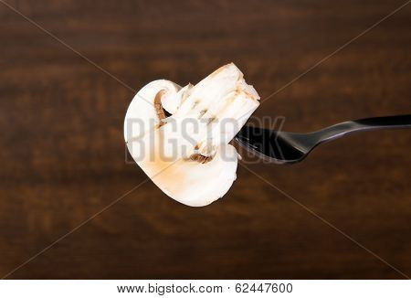 One sliced mashroom on a fork. Over wooden background.