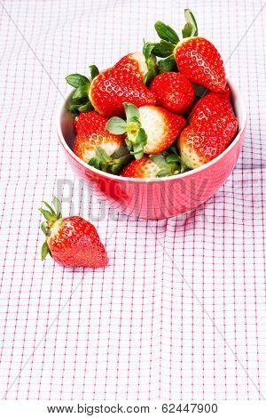 Fresh red strawberries in a bowl. Over kitches clothes background.