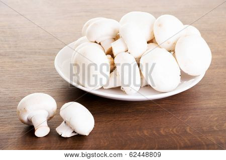 Fresh raw mashroom lying on a plate. Over wooden background.