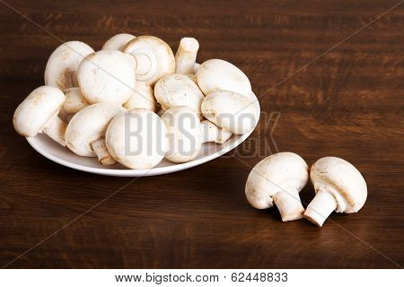 Fresh raw mashroom lying on a plate. Over wooden background.