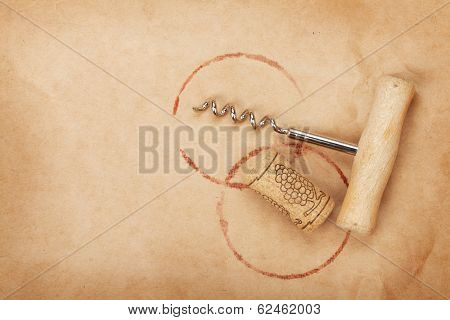Corkscrew and cork with red wine stains on brown paper background with copy space