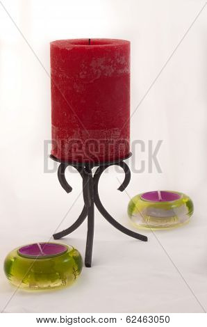 Red candle in a black forged candlestick holder  with two green tea light holders