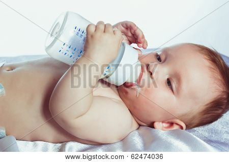 beautiful little girl with blue eyes lying on her back in diapers and holding a bottle of milk