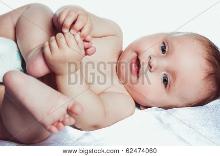 Baby in diapers holding his leg and smiling