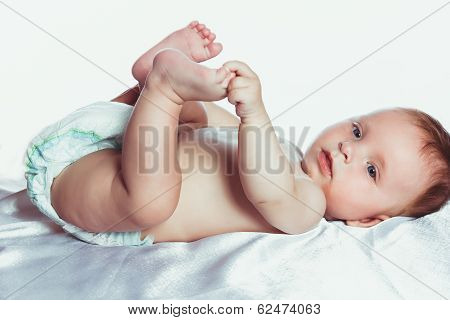 Cute baby in diapers holding his leg