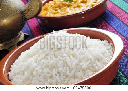 closeup of an earthenware bowl basmati rice and a bowl with korma curry in the background on a set table