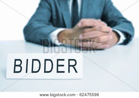 a man wearing a suit sitting in a desk with a desktop nameplate in front of him with the word bidder