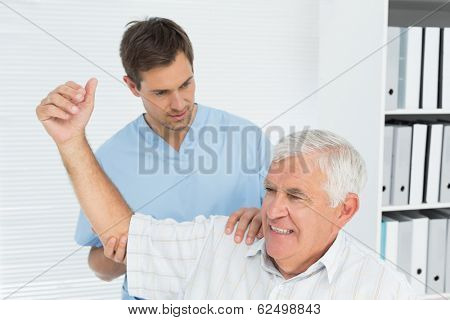 Male physiotherapist assisting senior man to stretch his hand in the medical office