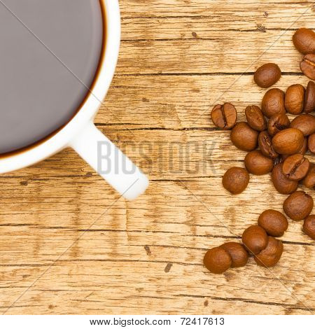 Close Up Of White Ceramic Coffee Cup With Roasted Coffee Beans On Wooden Table - View From Top