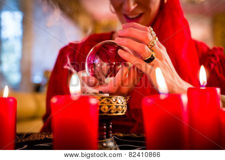 Fortuneteller or esoteric Oracle, sees in the future by looking into their crystal ball, incense burning and candles giving light