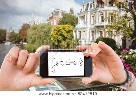 Composite image of hand holding smartphone showing je taime against canal scene