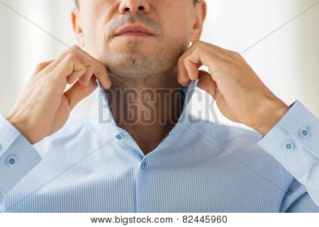 people, business, fashion and clothing concept - close up of man dressing up and adjusting shirt collar at home