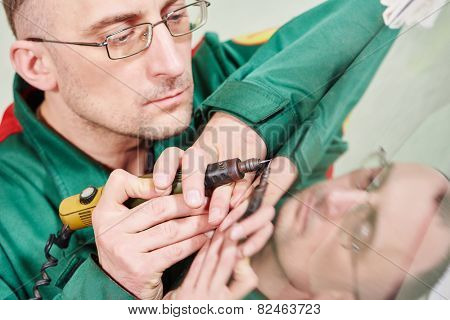 Automobile glazier repairman at windscreen repair of a car in auto service station garage