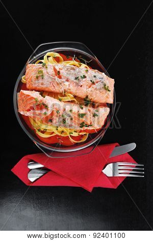 fresh fried natural pink salmon on italian traditional tagliatelle backed with tomato and vegetables served over black wooden table