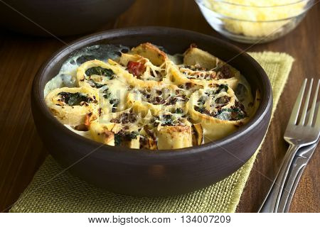 Baked crepe rolls casserole filled with spinach tomato and mincemeat with cream sauce and grated cheese on top served in rustic bowl photographed with natural light (Selective Focus Focus on the front of the middle roll)