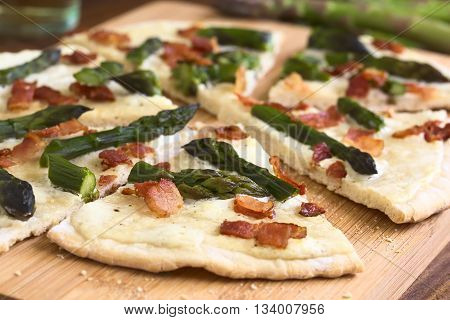 Green asparagus and bacon tarte flambee or Flammkuchen a typical Alsatian and South German dish photographed on wooden board with natural light (Selective Focus Focus one third into the image)