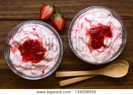 Strawberry fool an English dessert made of whipped cream and stewed strawberries served in glass bowls photographed overhead on dark wood with natural light (Selective Focus Focus on the top of the desserts)