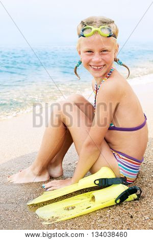 Happy little child smiling on summer beach sand with snorkel equipment looking to side at copy space after swimming with fins and mask on vacation.