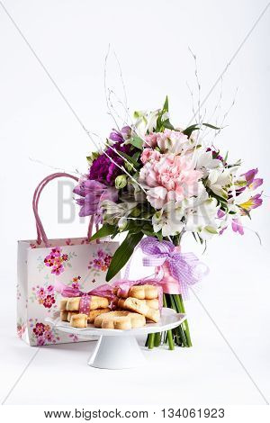 Pastel bouquet from pink and purple gillyflowers and alstroemeria on white background with gift and cookies