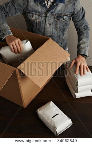 Bearded Brutal Man In Jeans Work Jacket Puts Blank Sealed Hermetic Packages Inside Big Carton Paper