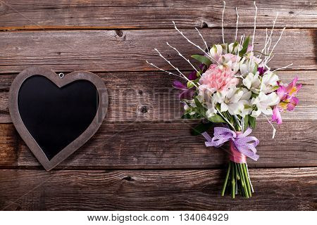 Rustic bouquet from gillyflowers and white alstroemeria on old rustic wooden background with wooden heart