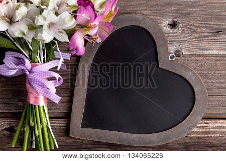 Rustic bouquet from gillyflowers and white alstroemeria on old rustic wooden background with wooden heart top view