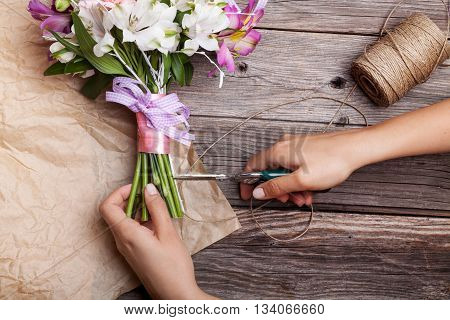 Making a rustic bouquet from gillyflowers and white alstroemeria on old rustic wooden background with wooden heart and scissors with paper