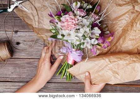 Packing a rustic bouquet from gillyflowers and white alstroemeria on old rustic wooden background with wooden heart and scissors with paper