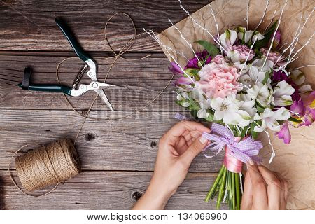 Making a bouquet from gillyflowers and white alstroemeria on old rustic wooden background with wooden heart and scissors with paper