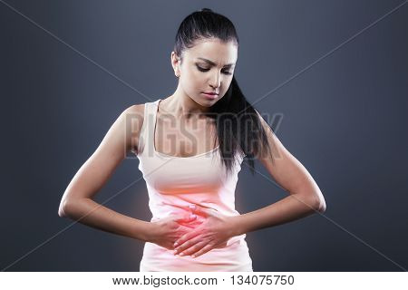Body pain. Studio shot of beautiful young woman with dark brown hair. Woman suffering from stomach pain. Red spot on stomach