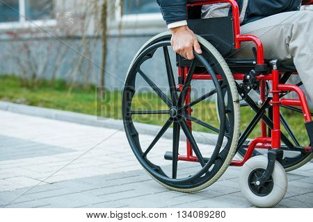 Adult man in wheelchair. Close up photo of male hand on wheel of wheelchair during walk