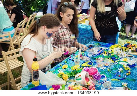 Zaporizhia/Ukraine- June 5, 2016: teen girls making wreaths and bracelets using artificial flowers, colorful ribbons and beads at handicraft workshop on charity family festival organized in regions with most quantity of refugees from Donetsk area, occasio