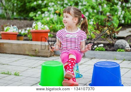 Little girl having fun in the summer garden pretending that she plays the drums using a plastic bucket
