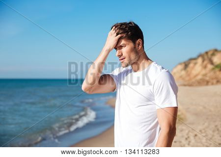 Serious attractive young man standing on the beach