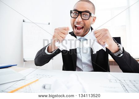 Angry businessman tearing up a document, contract or agreement in office