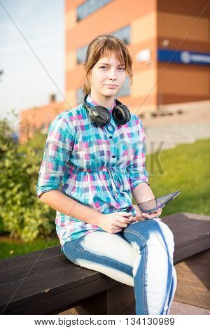 Preparing to exams outdoors. Beautiful young female student writing or reading something from note pad.  Woman sitting on bench in city park.