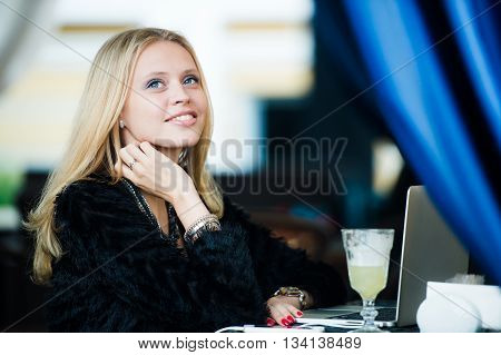 Young gorgeous European woman with pretty face thinking about something while sitting with laptop computer in cafe bar, dreamy beautiful female using portable net-book during work break in coffee shop