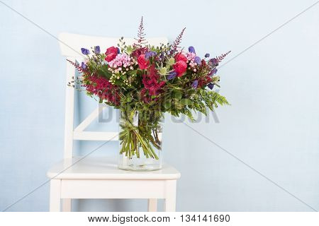 mixed bouquet flowers in vase on chair with blue background