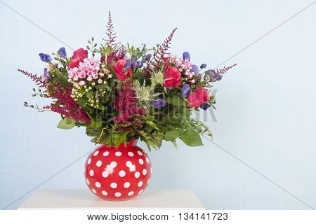 Red dotted vase with mixed bouquet flowers on blue background