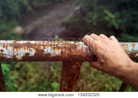 Male hand gripping to a rusty river bridge fence concept of suicidal tendencies jumping over the edge.