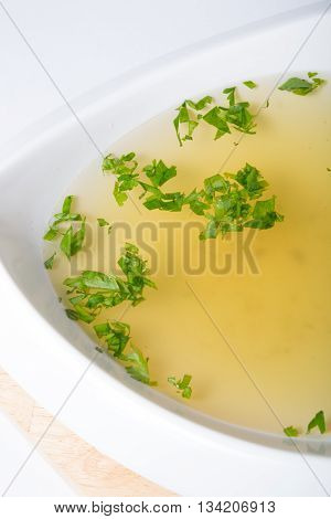Yellow broth with herbs in a white bowl