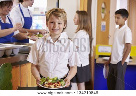 Blonde haired boy holding plate of food in school cafeteria