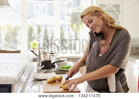 Busy Mother With Baby In Sling Multitasking At Home