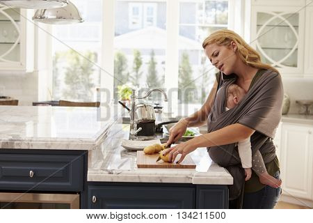 Busy Mother With Baby In Sling Multitasking At Home