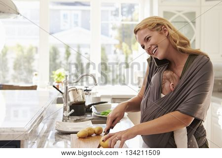 Busy Mother With Baby In Sling Multitasking At Home