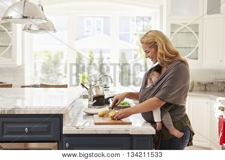 Busy Mother With Baby In Sling Multitasking At Home