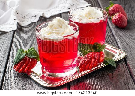 Delicious strawberry jelly with whipped cream in a glass and ripe strawberries on a metal plate on dark wooden table. Selective focus