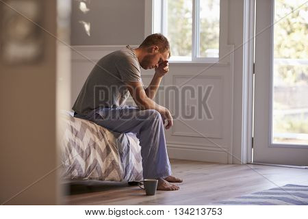 Man Wearing Pajamas Sitting On Bed With Head In Hands